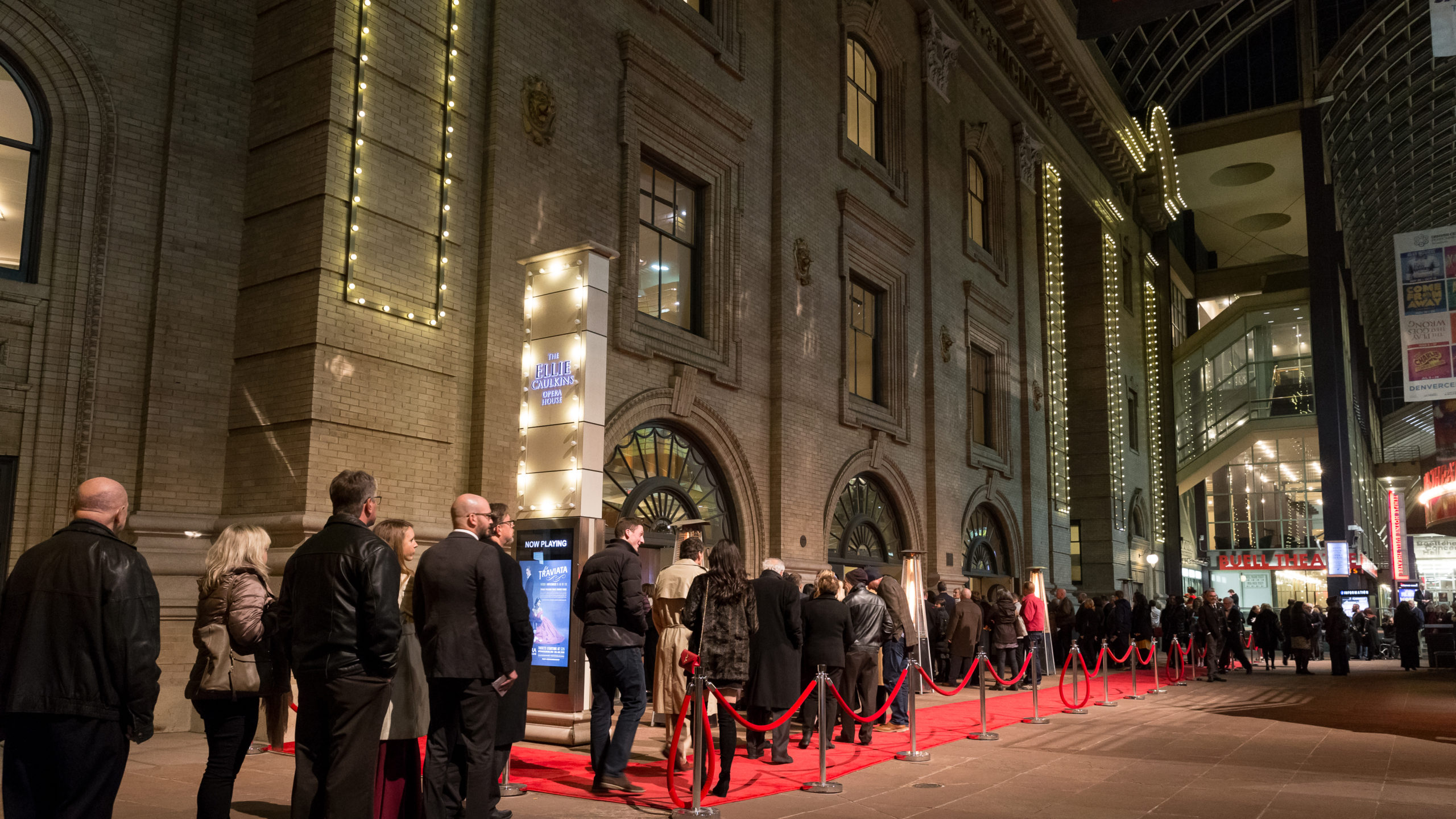 A long queue of patrons walk the red carpet in front of the Ellie Caulkins Opera House