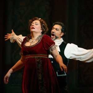 Luis Ledesma (Scarpia) stands behind Melissa Citro (Tosca) and sings threateningly at her.