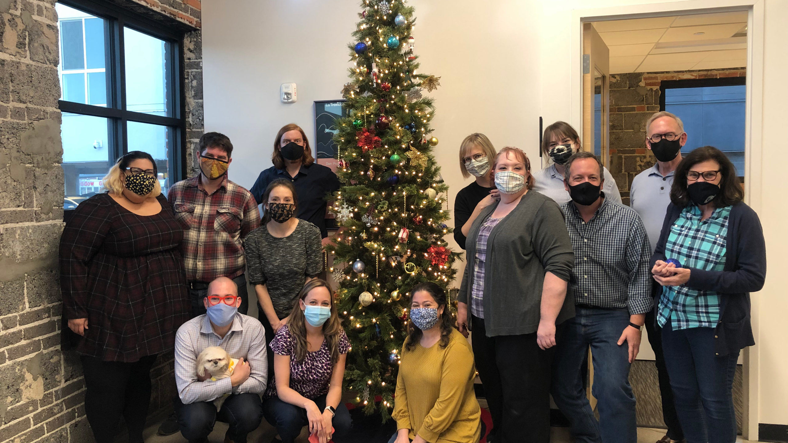 The Opera Colorado staff stand around the office Christmas tree smiling