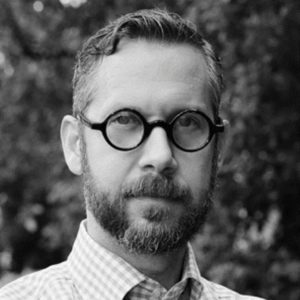 Headshot in black and white of a man with a beard and glasses
