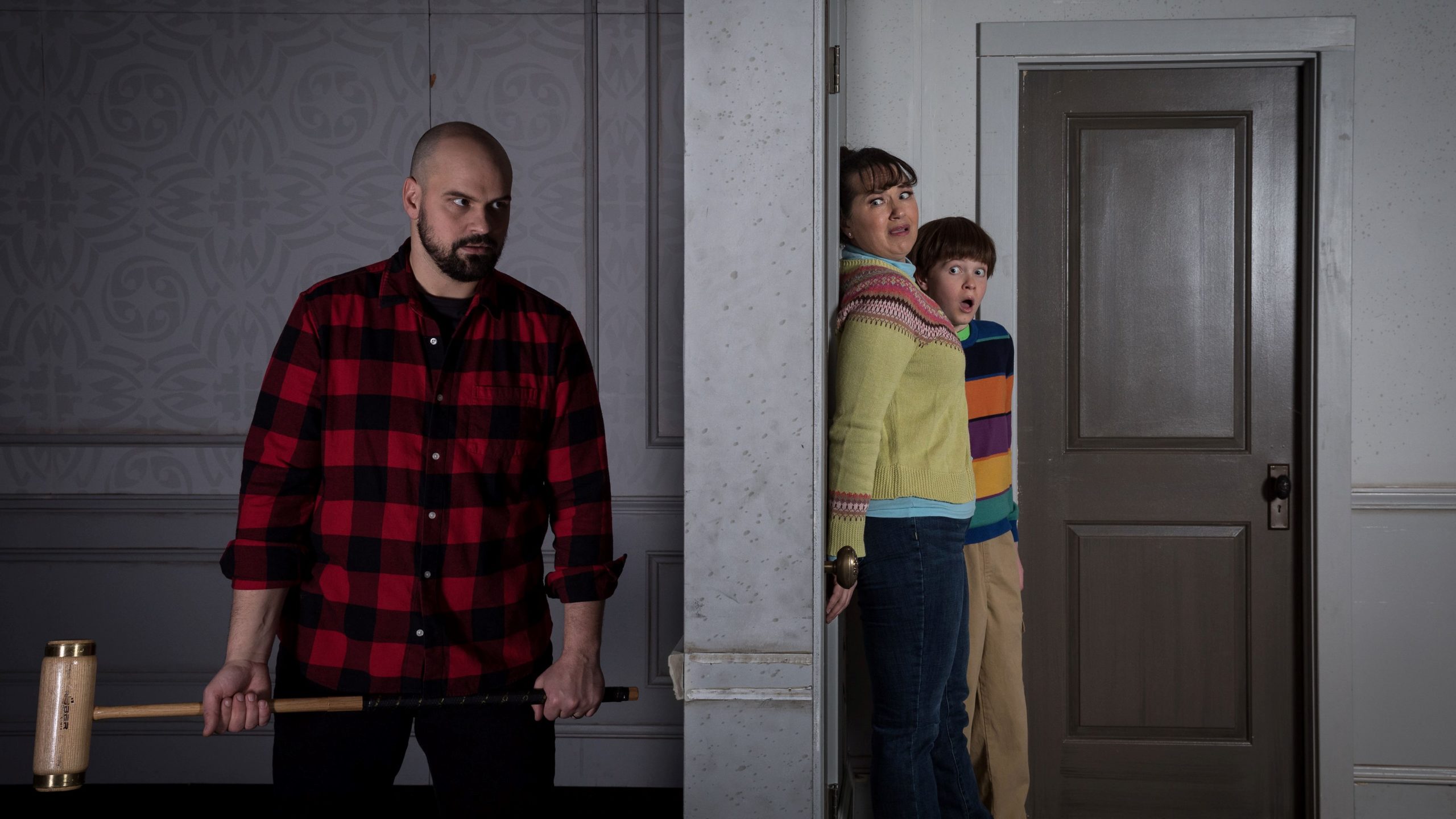 Scene from The Shining with Jack on one side of a door, trying to push through to the other side with Wendy and Danny barricading the door