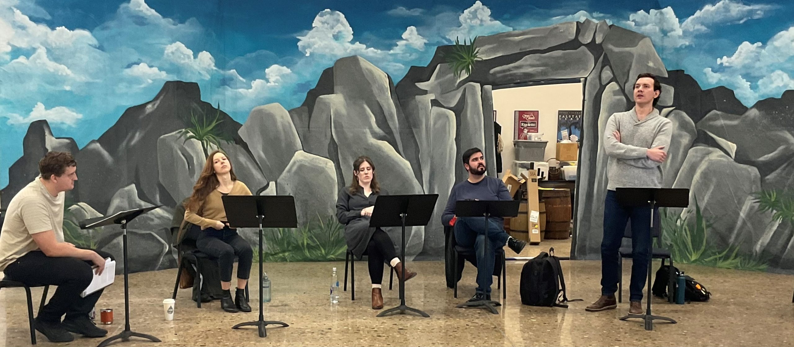 The Opera Colorado Artists in Residence sit in front of the rocky cove set for Pirates to rehearse