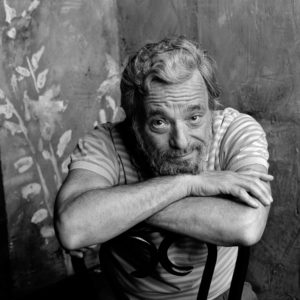 Black and white image of a Stephen Sondheim sitting with his arms crossed over the back of a chair