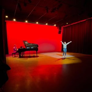 Kate Aldrich (Carmen) performs in front of a red light backdrop with a grand piano.