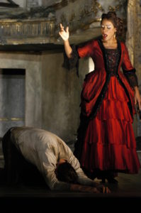 Denyce Graves as Carmen stands in a red dress over a kneeling Don Jose.