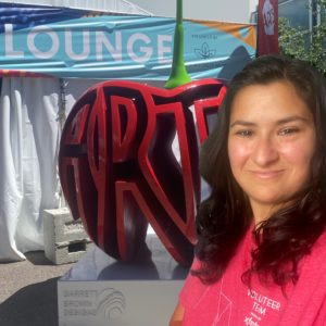 A woman in a red shirt stands on the right side of the image. A red sculpture shared like a cherry with the word “art” in the center is in the background.