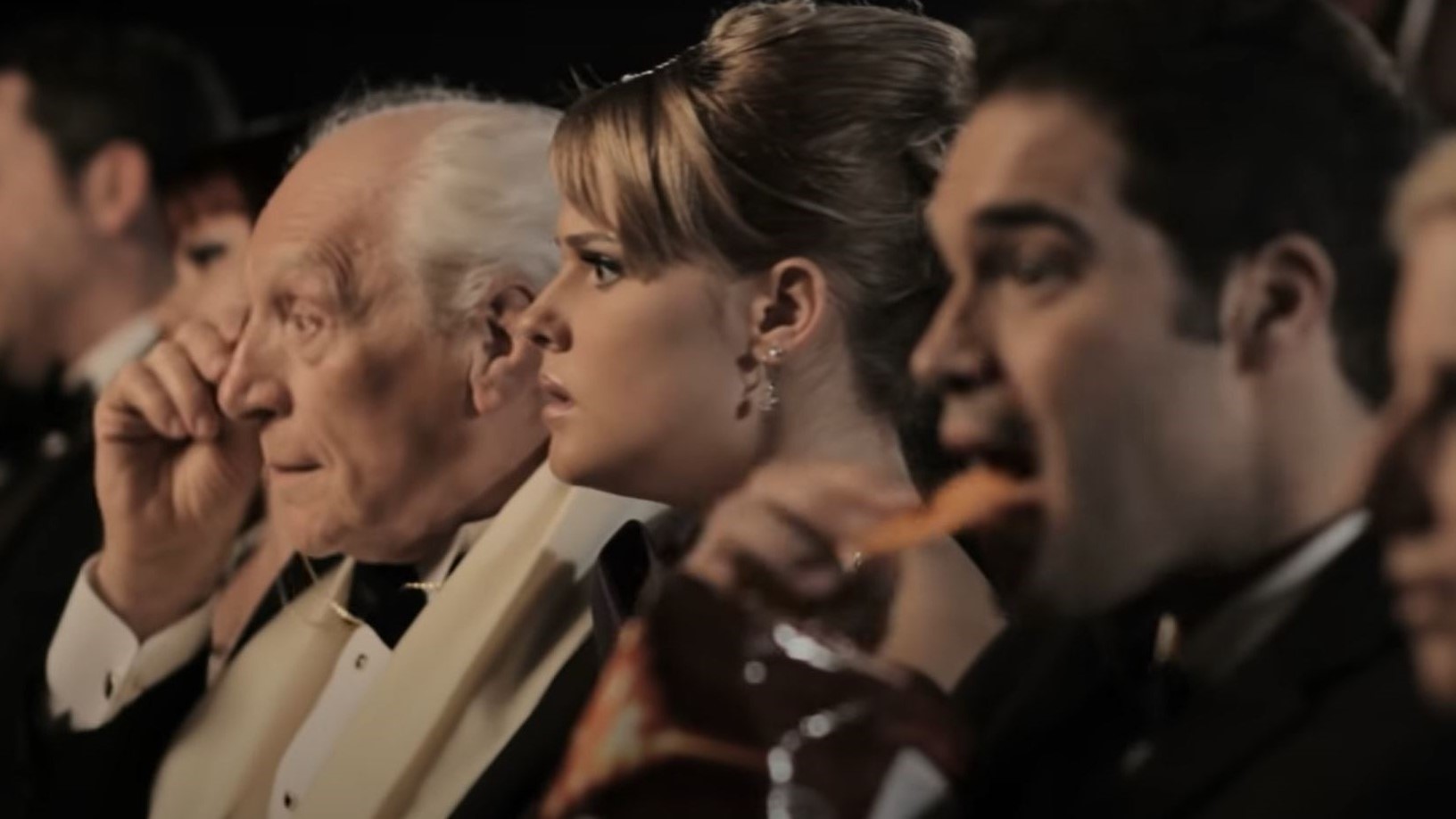 A man in the audience of an opera munches loudly on Doritos. Other opera patrons look on with frustration.