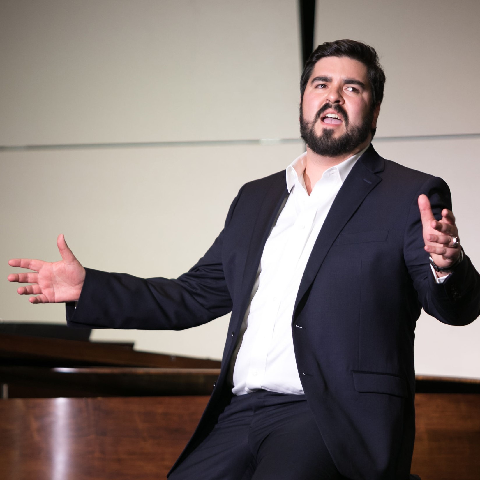 Baritone Thomas Lynch sits in the crook of the piano performing a song.