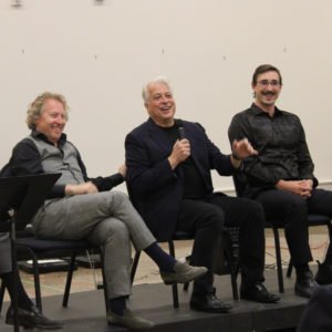 Three men sit on a platform smiling and laughing.