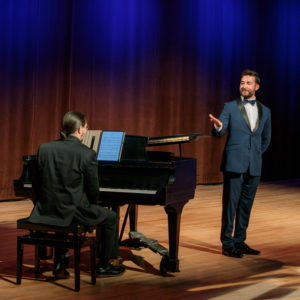 A man in a blue suit performs in front of a piano