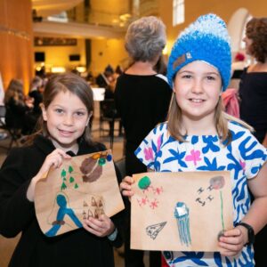 Two girls hold up brown papers with drawings