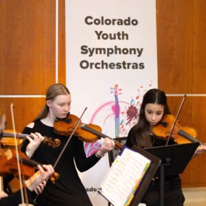 Two people in all black outfits play the violin