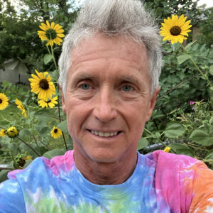 Headshot of a man with a tye-dye shirt in front of sunflowers