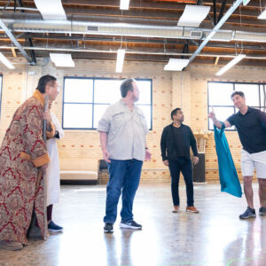 Four men stand together in a rehearsal hall