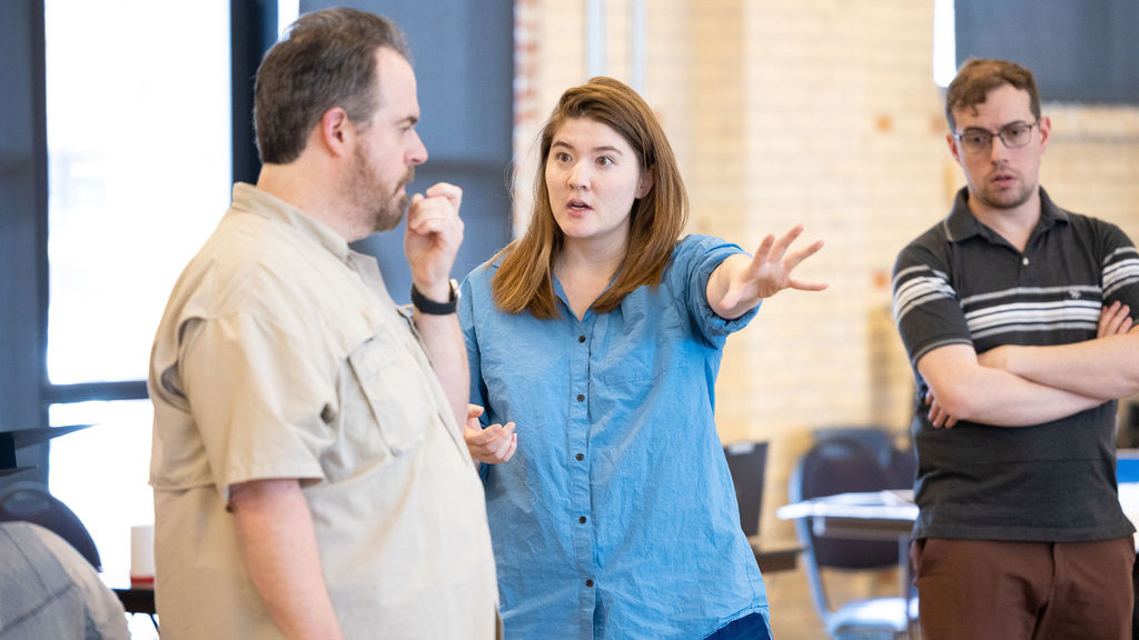 A woman in a blue shirt points to something in the distance for a male coworker to see