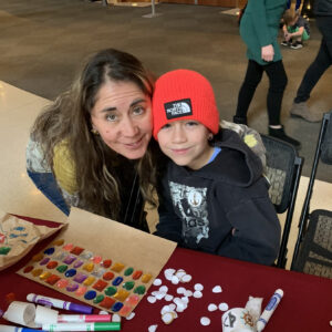 A woman next to a young boy sitting at a table with craft supplies