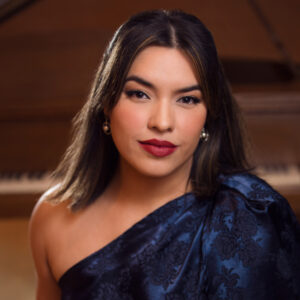 A woman with dark hair and a blue and black dress smiles at the camera