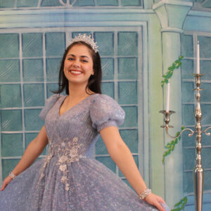 A woman wearing a blue dress and tiara poses.