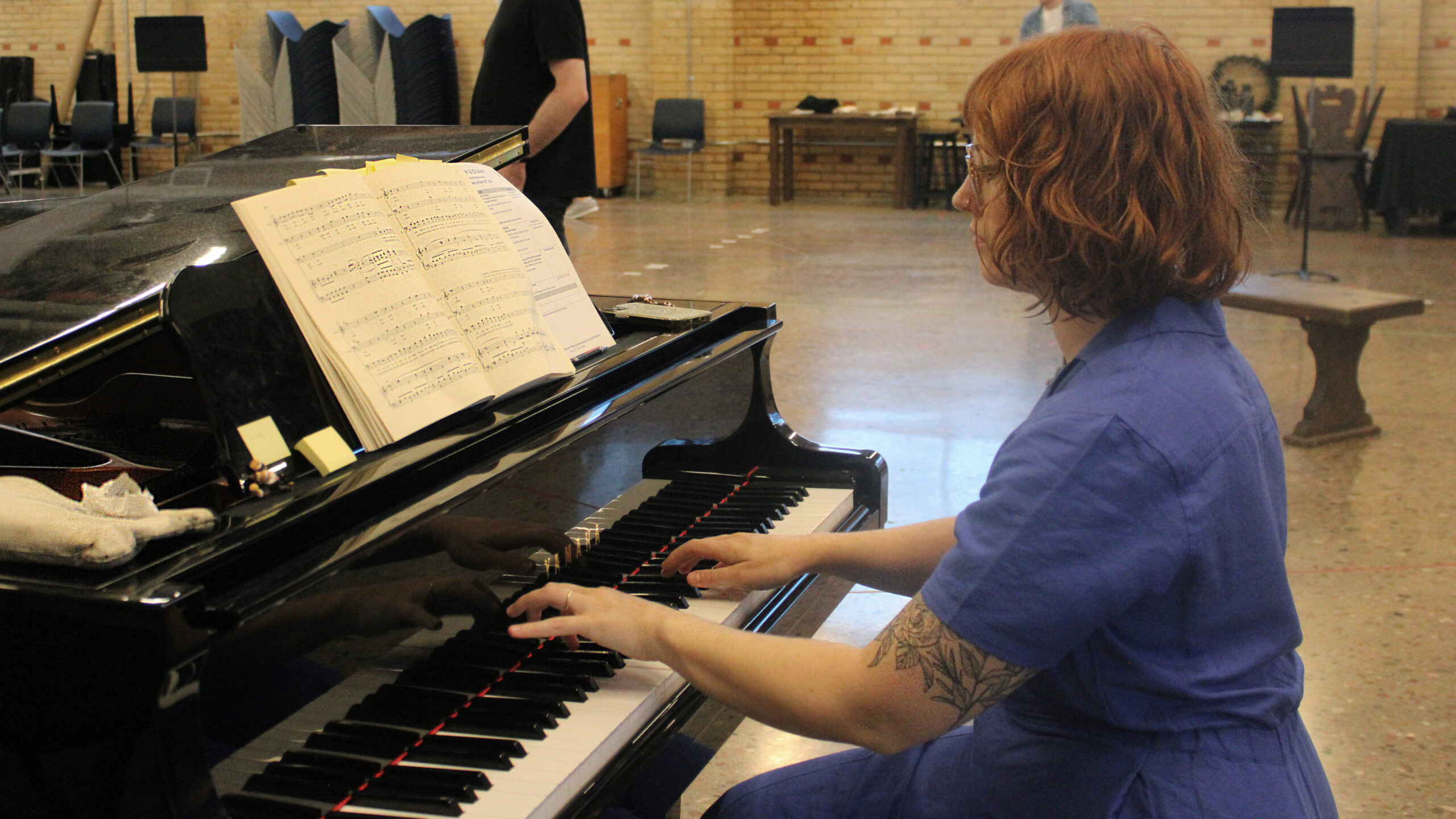 A woman in blue plays the piano in a rehearsal hall