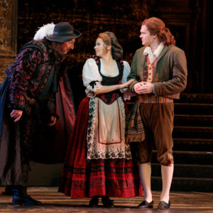 A man in rich clothes talks to a young couple, a man and woman, in more simple attire