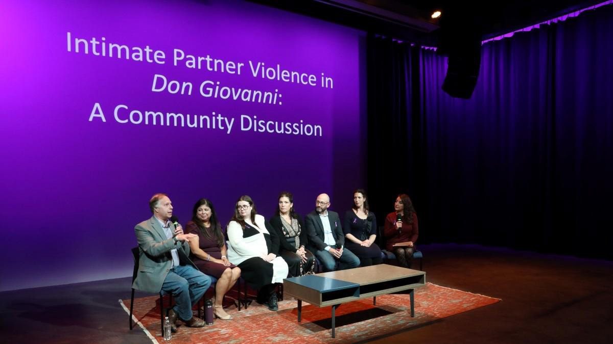 A group of people sit in a row in front of a purple screen reading Intimate Partner Violence in Don Giovanni: A Community Discussion