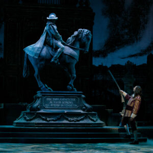 A man faces a statue of a man on a horse at night