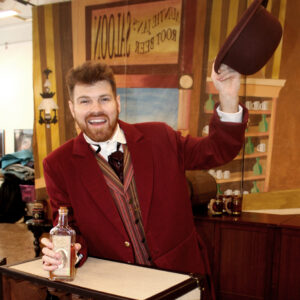 A man in a red suit tips a hat and holds a large glass bottle