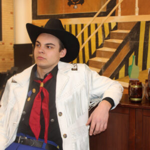 A man in a black cowboy hat and a white fringe jacket