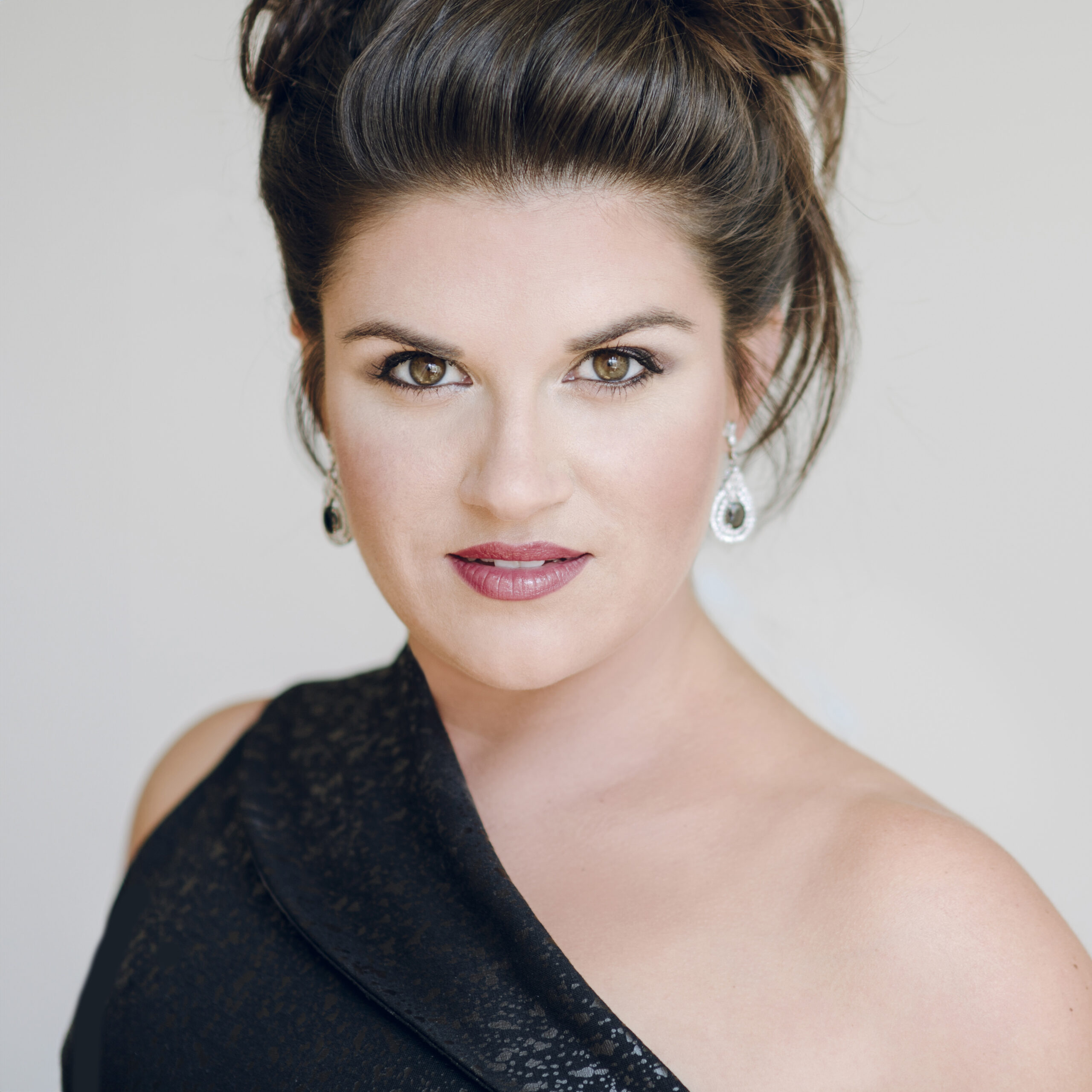 Headshot of a woman with black hair bundled on top of her head wearing a black dress