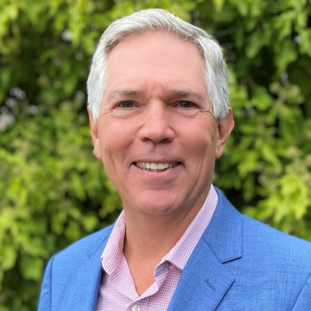 A man with white hair and a blue suit smiles at the camera