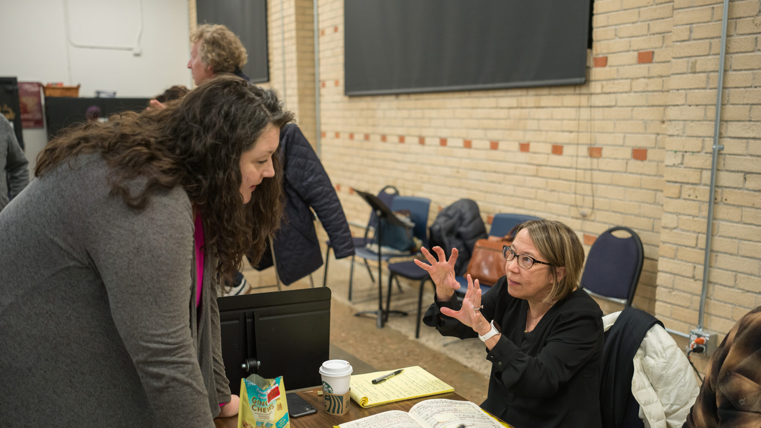 Two women talk over a table with notes