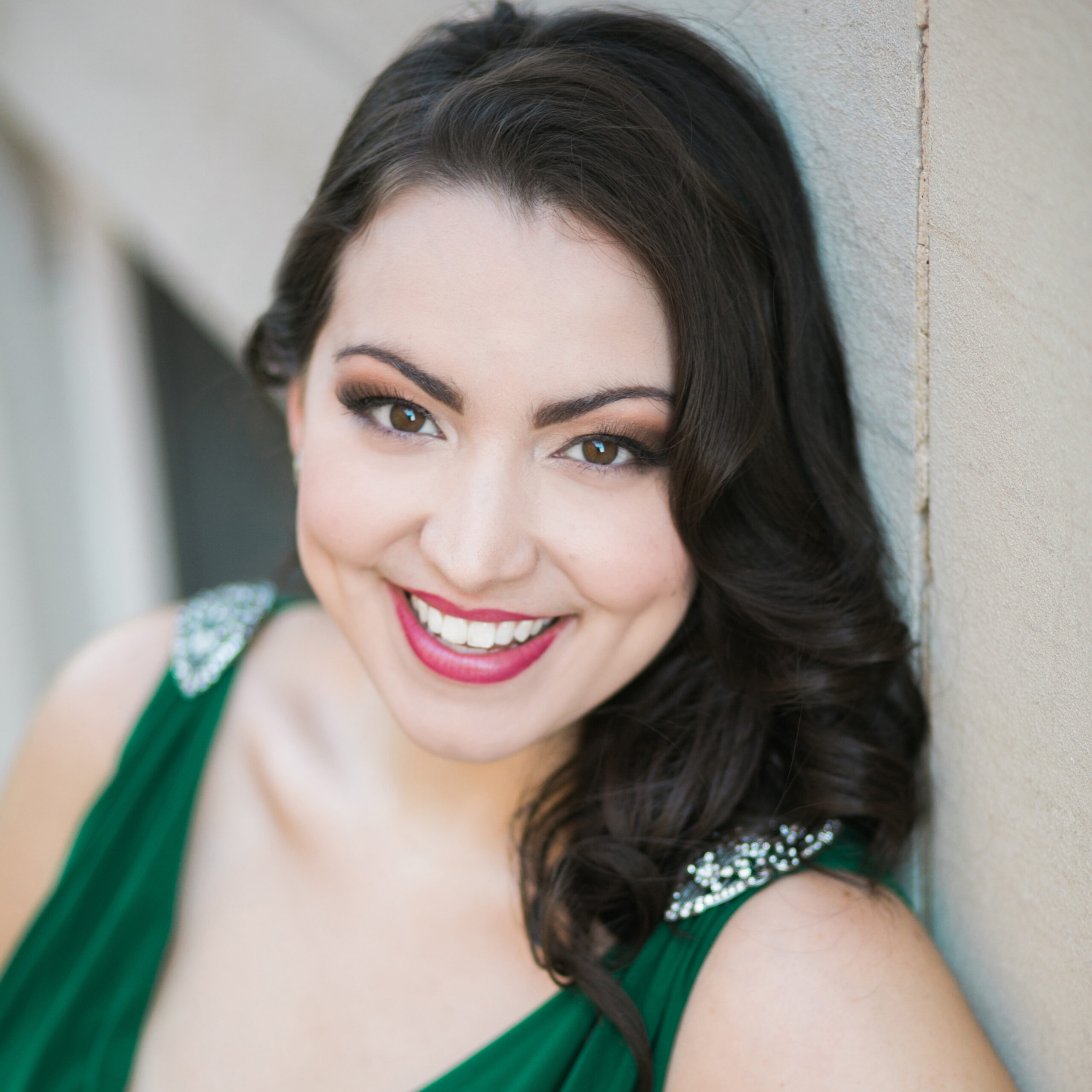 Headshot of a woman with dark black hair wearing a green dress smiles at the camera