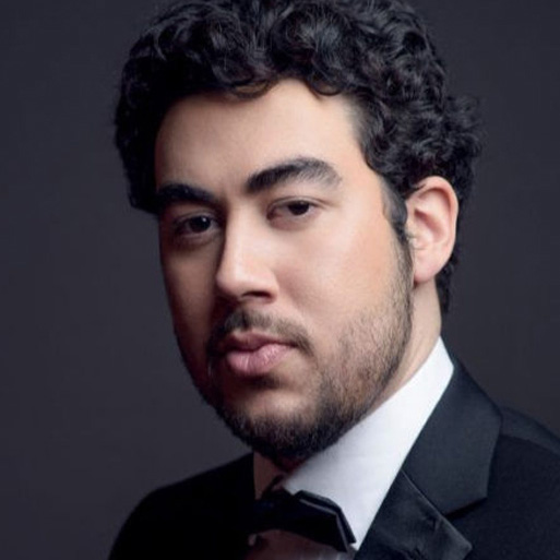 Headshot of a man with dark curly hair and a black suit