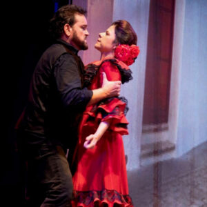 A man wearing all black holds a woman in a red dress