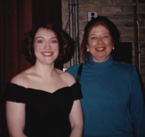 Two women, one in black, one in blue, smile at the camera