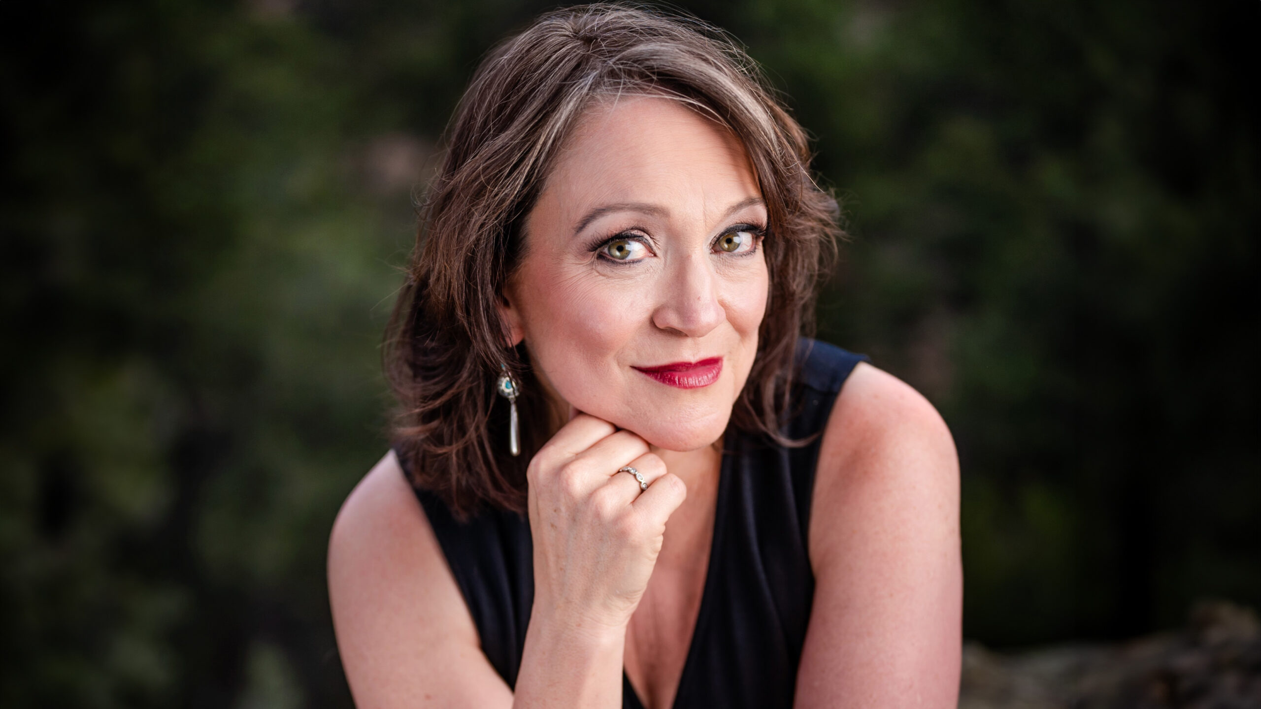 A woman smiles at the camera and rests her chin on her hand