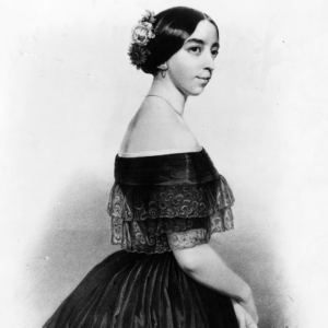 Black and white image of a woman in a black dress and white flowers in her dark hair in a bun.