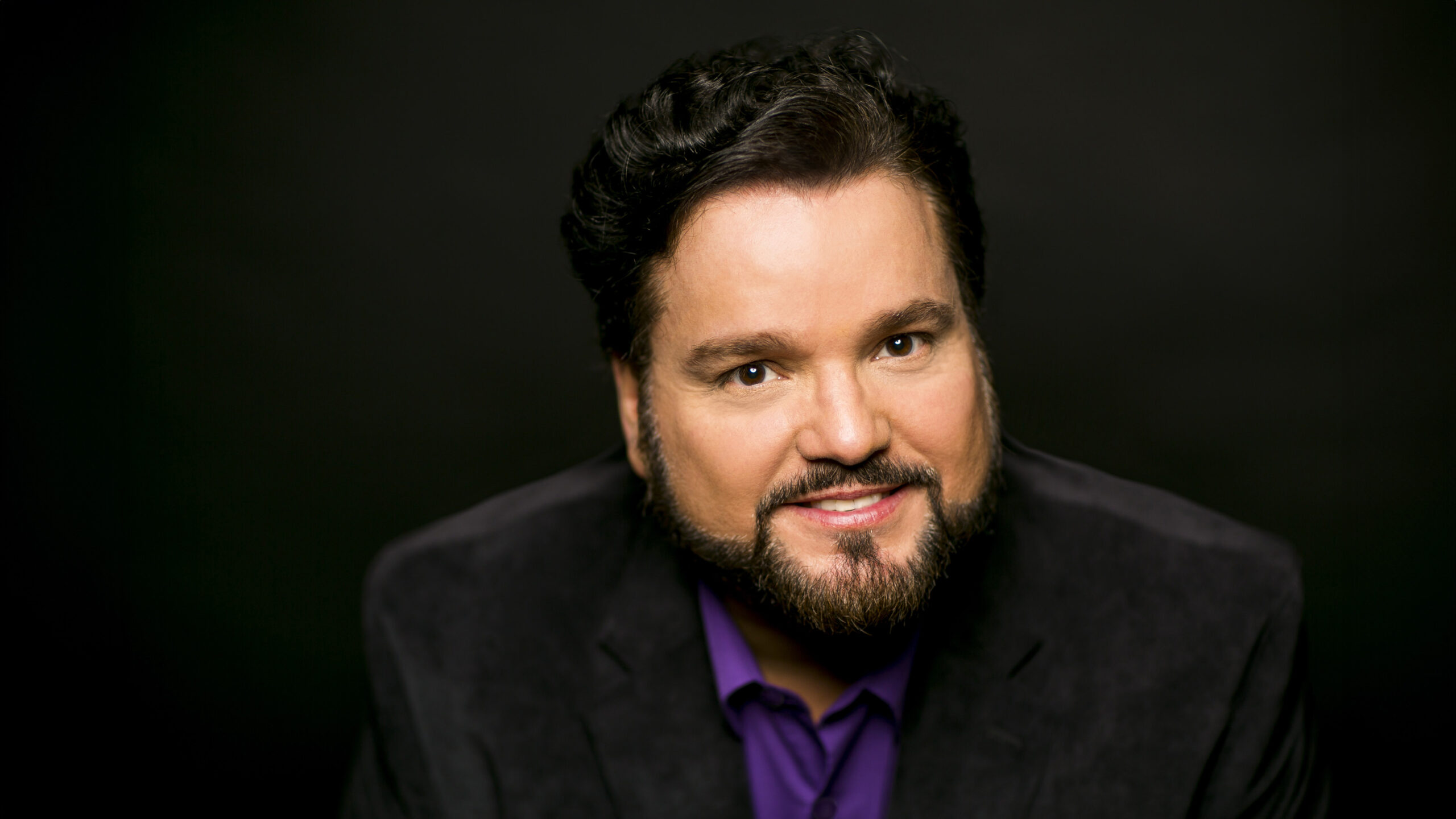 Headshot of a man with dark hair wearing a purple shirt and black suit